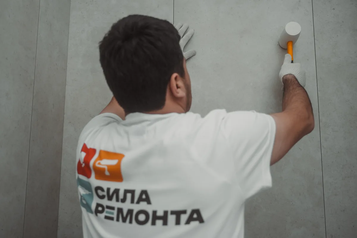 Плиточник осаживает крупноформатную плитку резиновым молотком